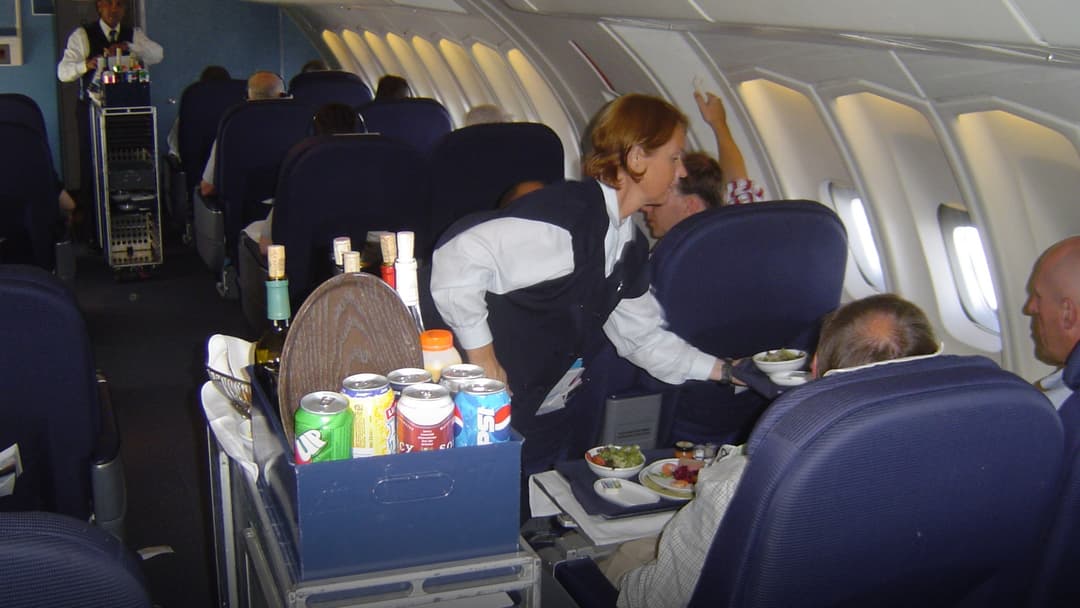 Flight attendant serving passengers beverages from an in-flight galley cart.