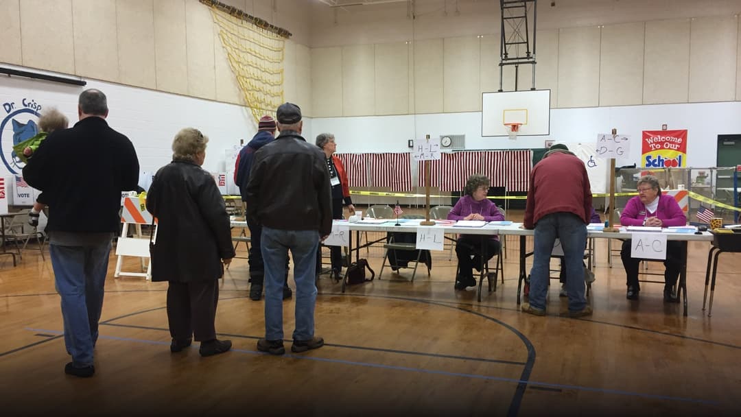 Voters filling out paper ballots at private voting booths inside an active New Hampshire polling precinct.