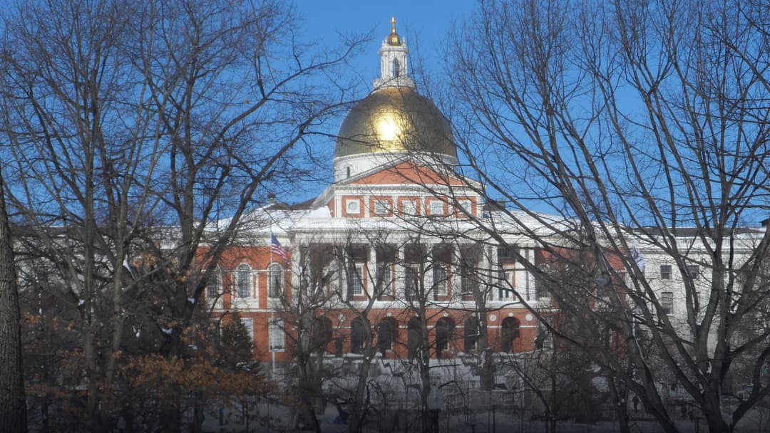 View of the Massachusetts State House and its golden dome across snowy park grounds in Boston.