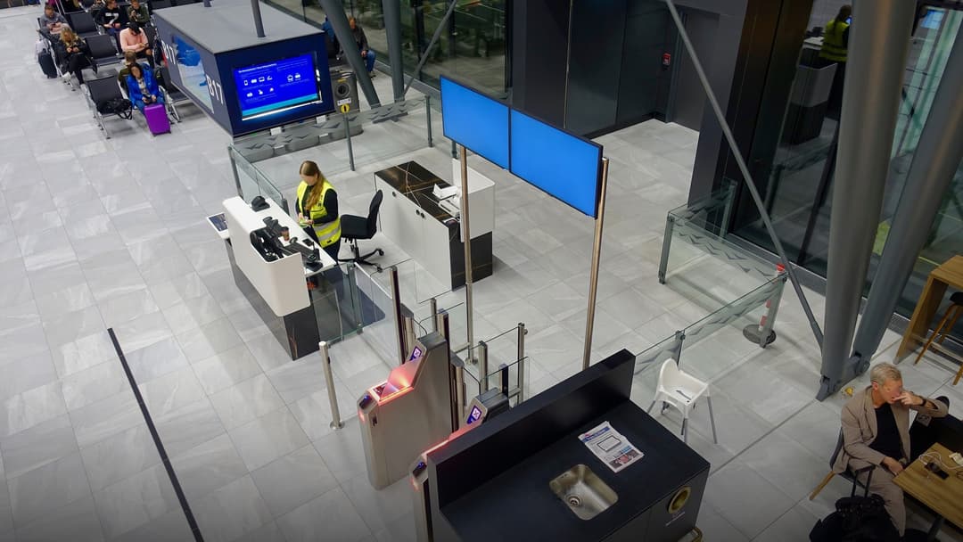 Crowd of airline passengers standing in front of airport boarding gate counters with luggage.