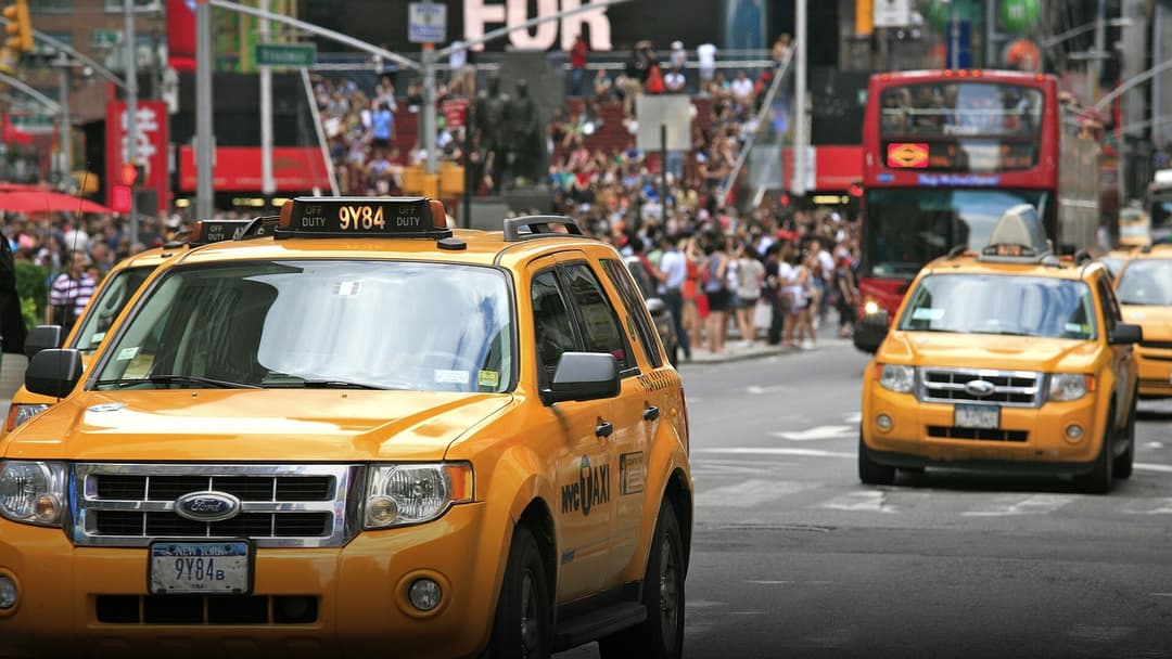 Line of iconic yellow NYC taxicabs driving through neon-lit Times Square at dusk.