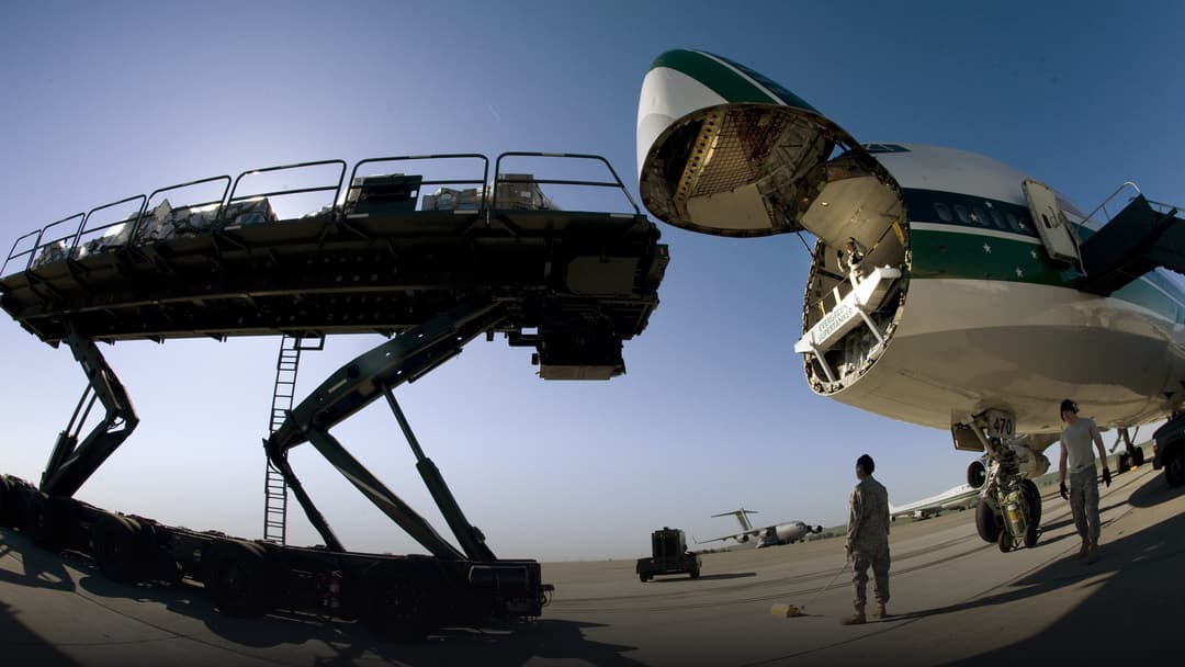 Commercial Boeing 747 freighter and military cargo aircraft loading pallets of freight on airport tarmac.
