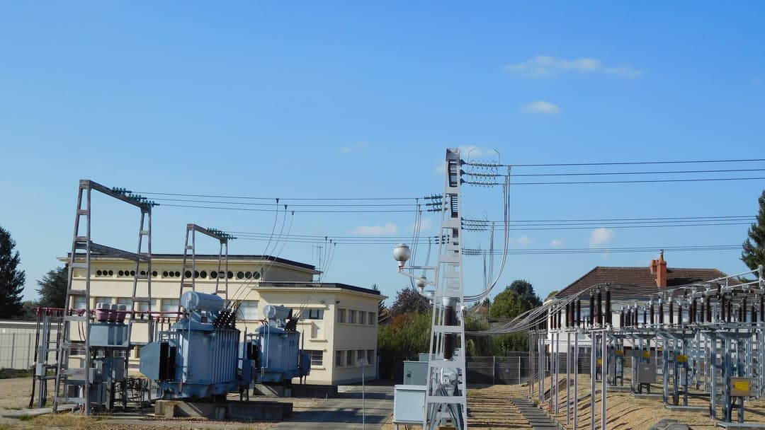 Massive high-voltage power substation transformers and transmission lines beneath a sprawling open sky.