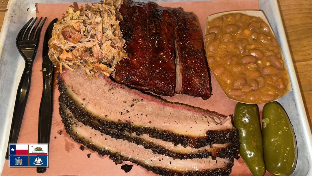 Grand Texas barbecue platter with smoked brisket, ribs, pulled pork, and US flag overlay in bottom-left corner