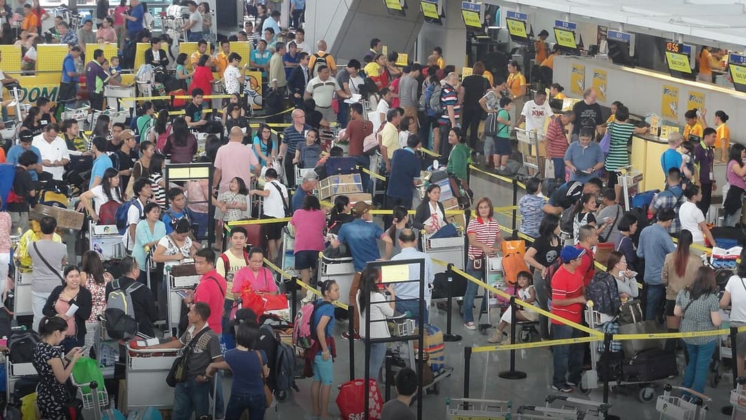 Massive crowd of airline passengers with luggage carts and baggage queueing in a busy airport departures hall.
