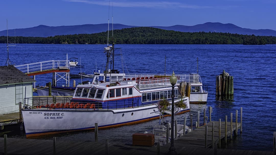 The historic M/V Sophie C U.S. Mail Boat docked at Lake Winnipesaukee with distant mountains in the background.