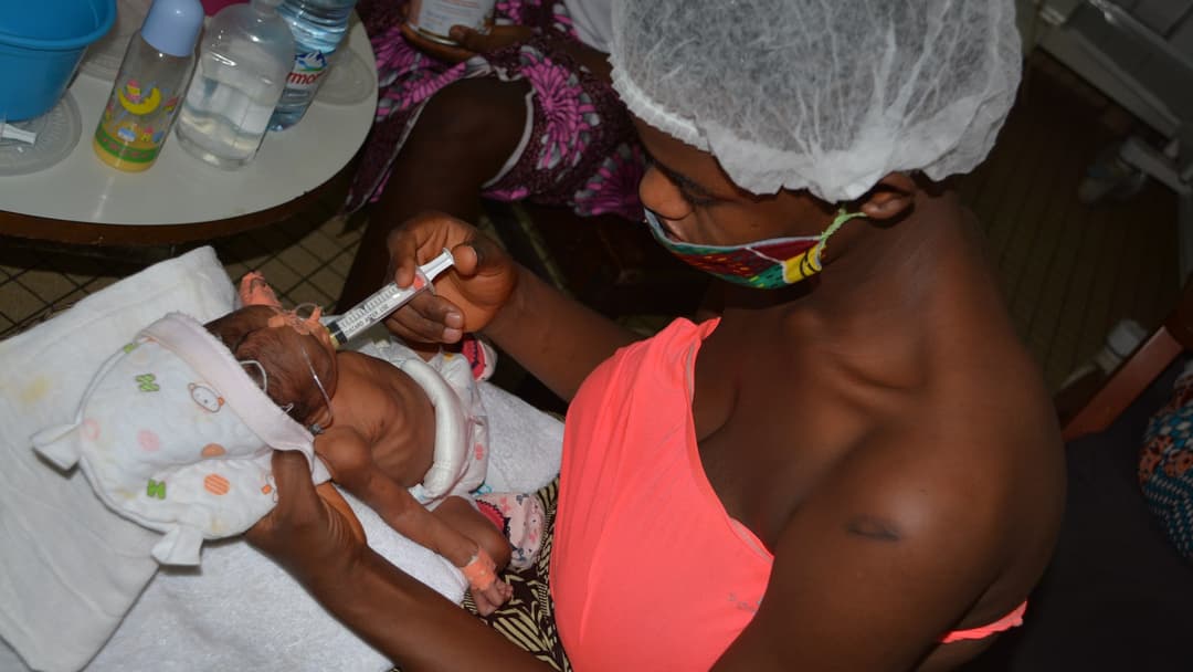 A mother holding and feeding her newborn infant in a hospital maternity room.