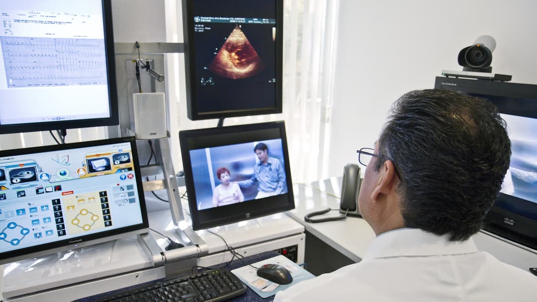 Physician conducting a remote telemedicine video consultation with diagnostic ultrasound and ECG monitors