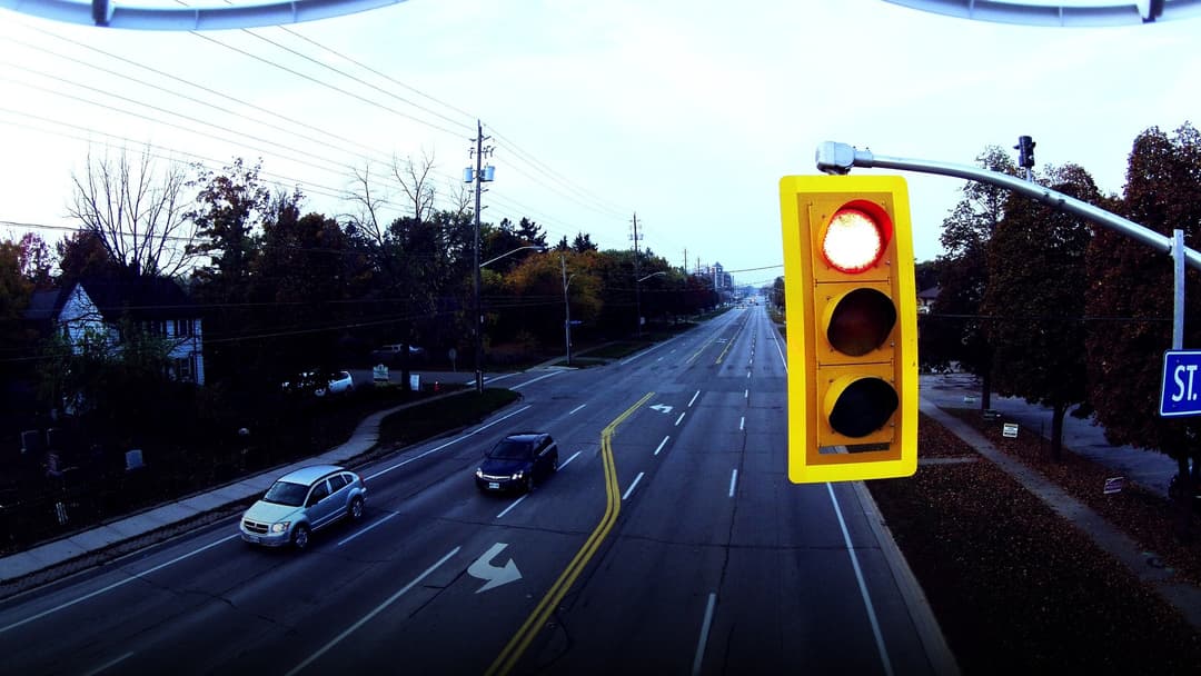 An elevated view of an American roadway intersection showing a prominent overhead yellow traffic signal glowing red above traffic lanes.