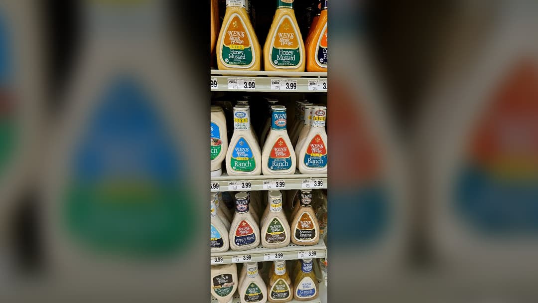Rows of bottled honey mustard, buttermilk ranch, and Caesar salad dressings on a grocery store shelf.