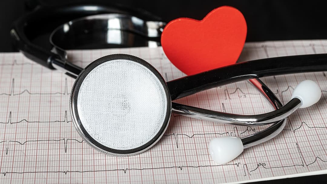 Medical stethoscope and red heart resting on an electrocardiogram chart.