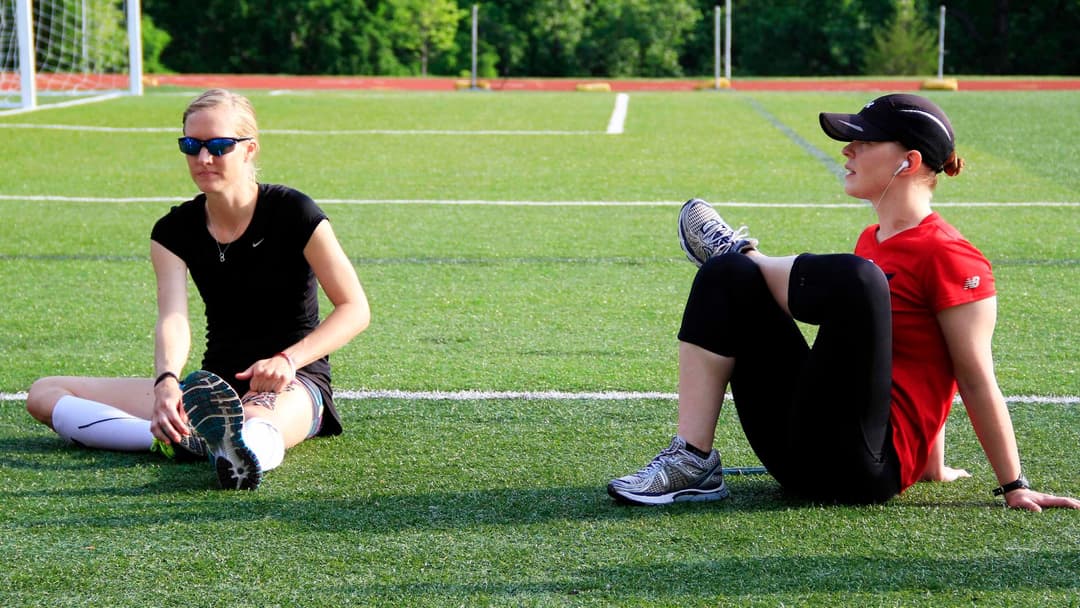 Athletes performing warm-up stretches on an athletic running track.
