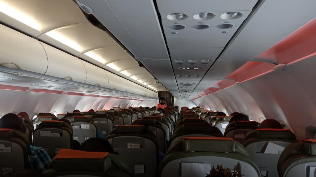 Commercial airliner cabin with passengers filling the center aisle under overhead bins.