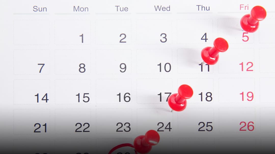 A printed monthly calendar grid with red pushpins marking days, showing Sunday as the first day of the week.