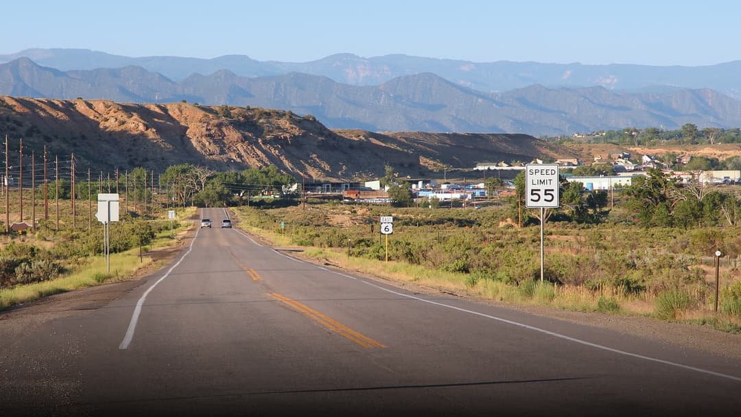 An American highway roadside sign reading Speed Limit 55 next to US Route 6 with mountains in the background.