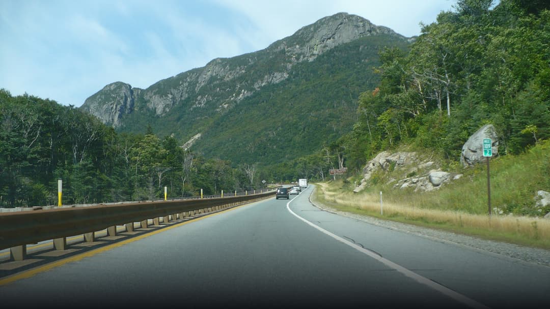Scenic view of Interstate 93 winding through Franconia Notch surrounded by towering autumn mountain peaks.