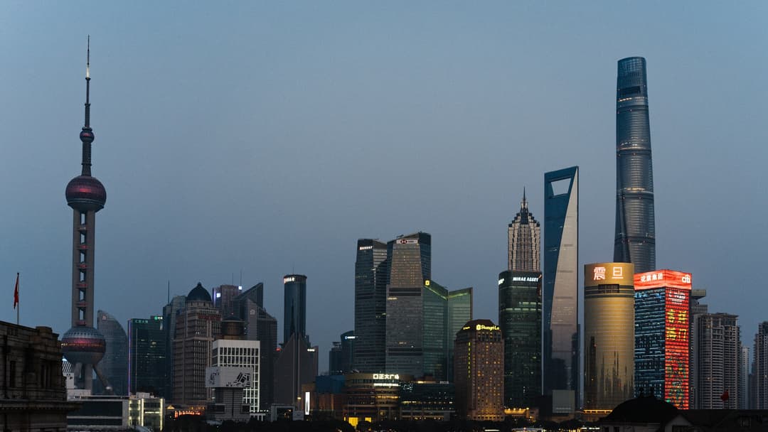 Illuminated high-tech skyline of Shanghai Pudong at twilight with neon reflections on the Huangpu River.