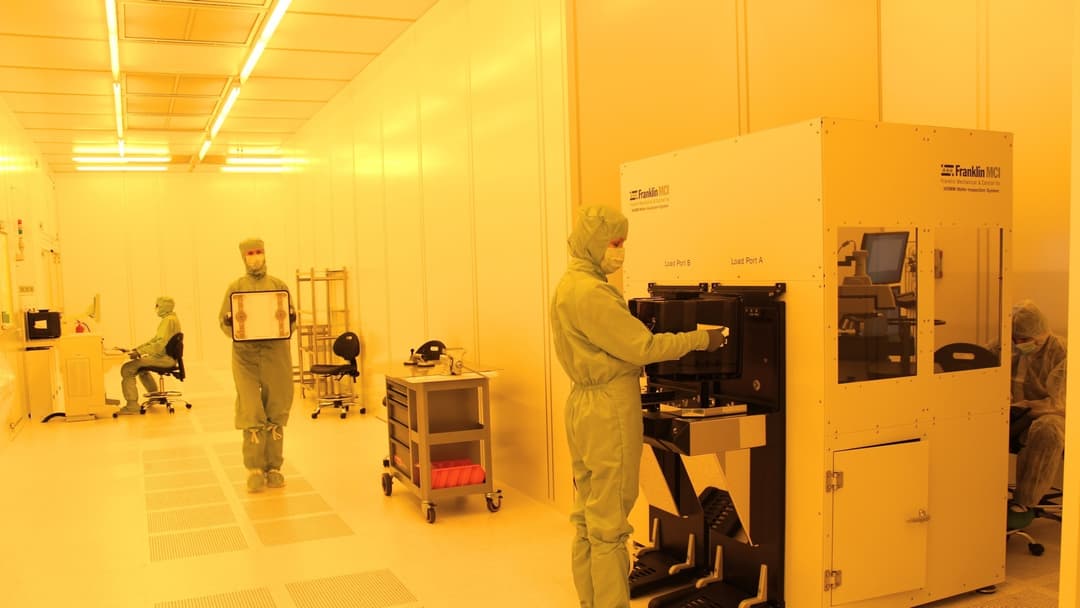 Photolithography semiconductor cleanroom technician in white bunny suit inspecting a silicon wafer.