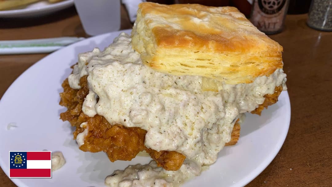 Golden fried chicken served over warm buttermilk biscuits and country gravy with Georgia flag overlay in bottom-left corner
