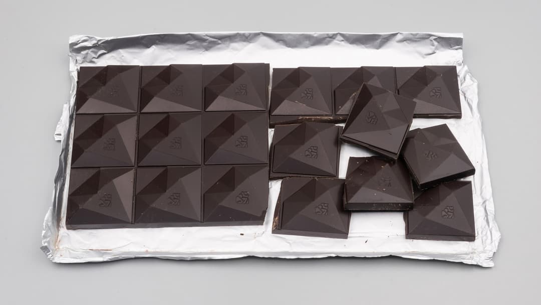 A bar of dark chocolate opened on silver foil with several geometric squares broken off.