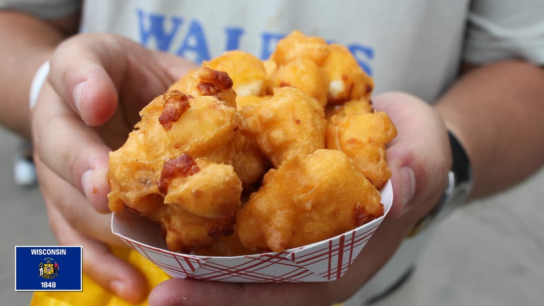 Basket of crispy golden deep-fried Wisconsin cheese curds with Wisconsin flag overlay in bottom-left corner