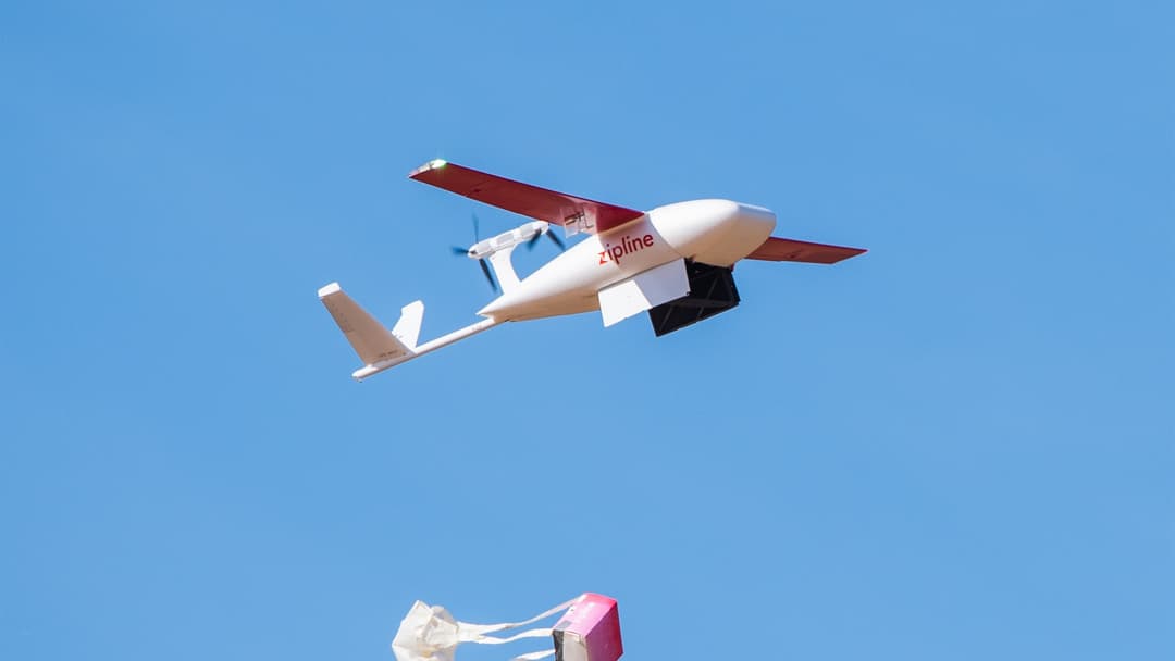 Zipline autonomous delivery aircraft releasing a medical supply package by parachute in mid-air