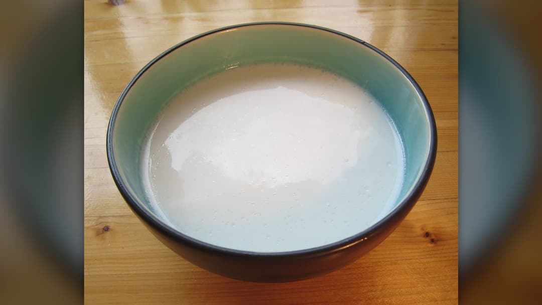 A ceramic bowl filled with thick white canned coconut milk on a wooden surface.