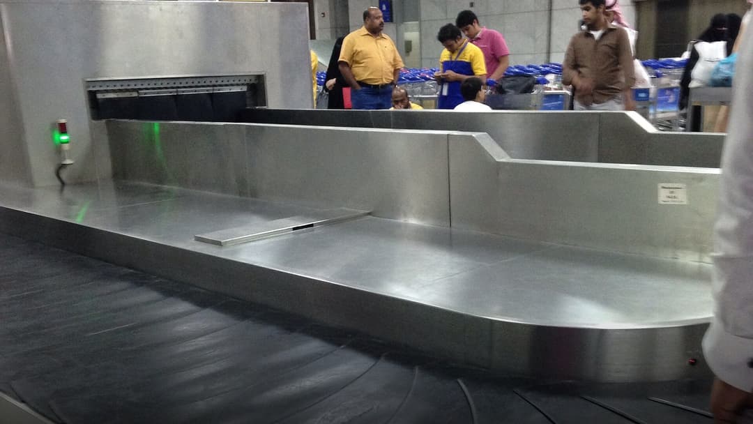 Airport baggage claim carousel with luggage bags rotating on the metal conveyor belt.