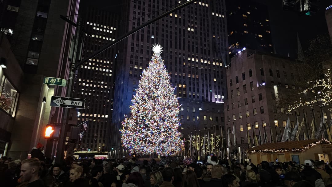 Illuminated Rockefeller Center Christmas tree towering over the holiday skating rink at night in Manhattan.