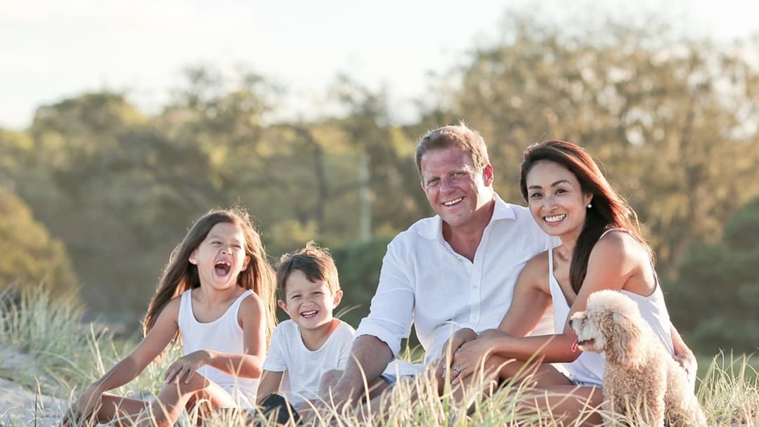 Parents and young children smiling together outdoors in matching white shirts