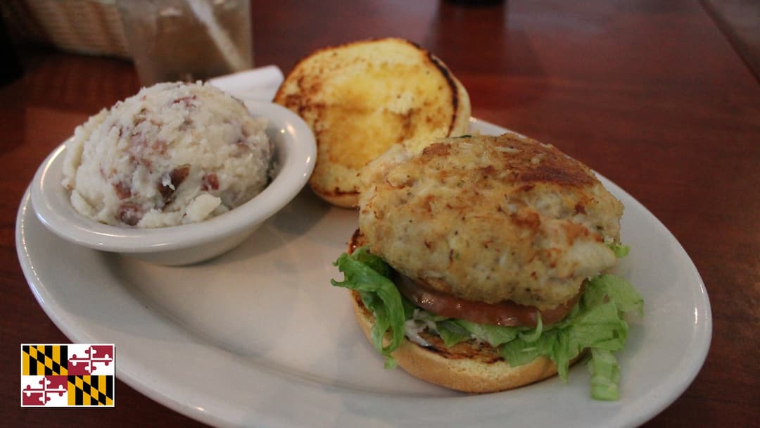 Golden pan-seared Maryland jumbo lump blue crab cakes with fresh lemon and Maryland flag overlay in bottom-left corner
