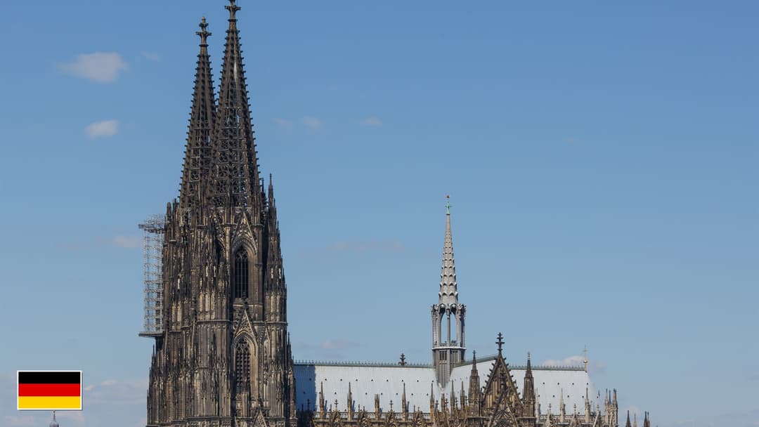 Cologne Cathedral twin 516-foot Gothic spires in Germany with flag of Germany in bottom-left corner