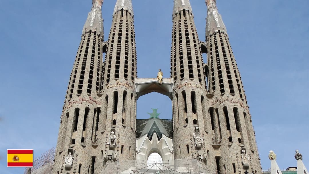 Sagrada Familia Passion Facade and four soaring bell towers in Barcelona with flag of Spain in bottom-left corner