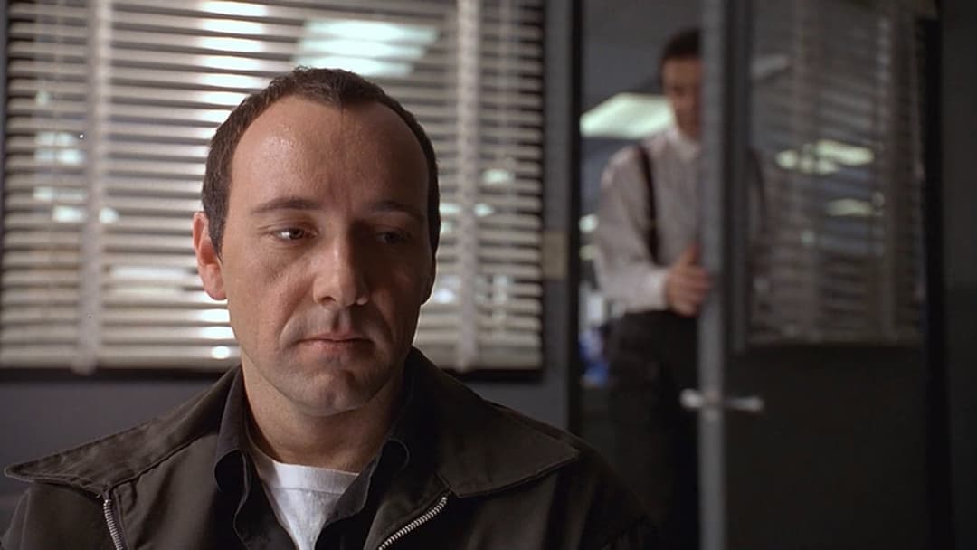 Verbal Kint looking downward with a pensive expression during police interrogation, image horizontally flipped.